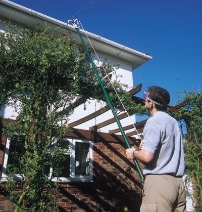 Hombre podando árbol usando pértigas de podar