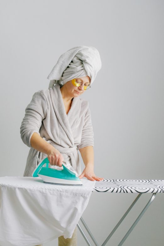 mujer en bata de baño planchando una camisa