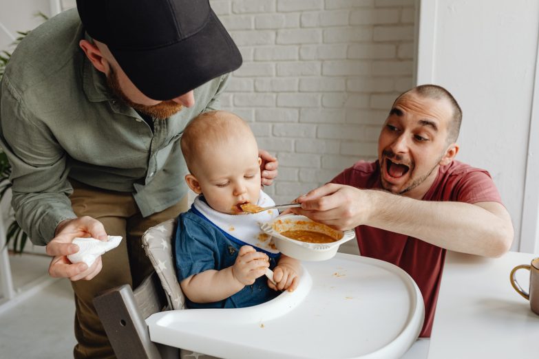 dos hombres dándole de comer a un bebé sentado en una trona para bebés