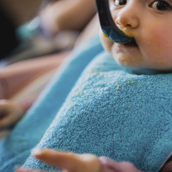 bebé comiendo con un babero de rizo en el cuello