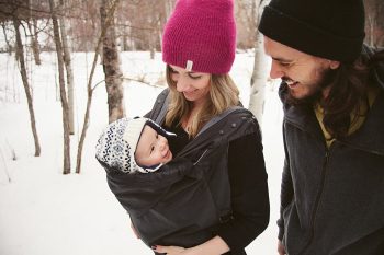 hombre y mujer paseando en la nieve con un bebé protegido con una funda portabebés