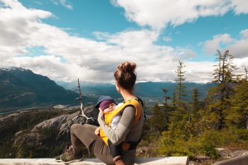 Mujer porteando a un bebé en un portabebés mientras está sentada observando la naturaleza