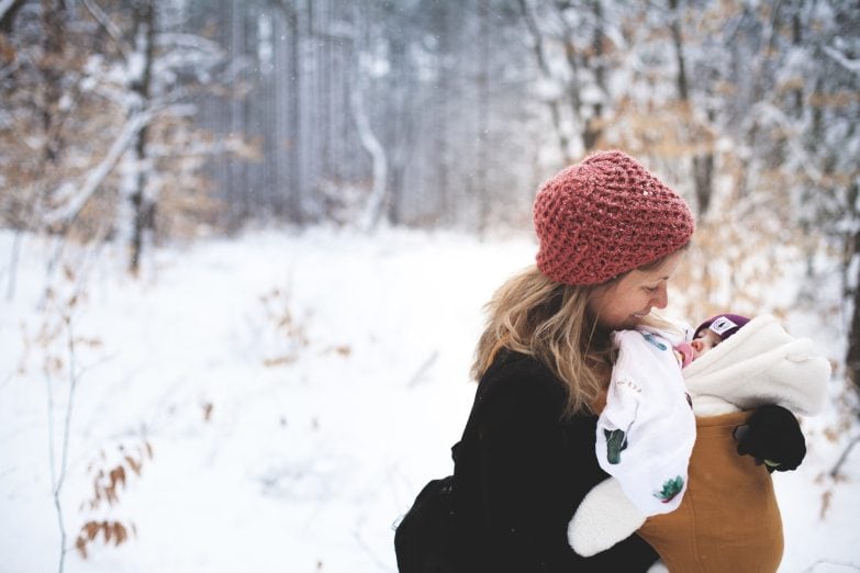 mujer porteando a un bebé protegido con una funda portabebés en un ambiente nevado