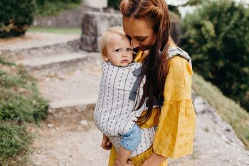 mujer delgada y pequeña porteando a un bebé en un portabebés