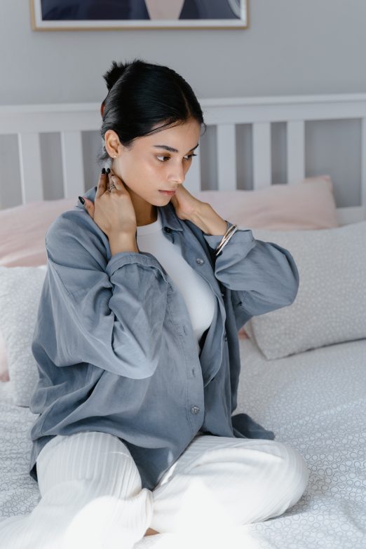 mujer sentada en la cama con dolor cervical